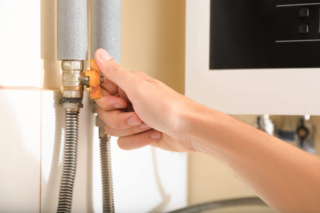 Man turning on valve of gas hot water heater indoors, closeup